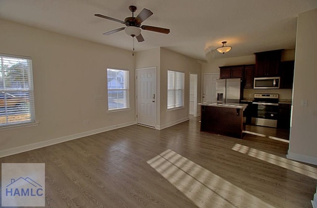 kitchen with a kitchen breakfast bar, a center island, ceiling fan, stainless steel appliances, and dark wood-type flooring