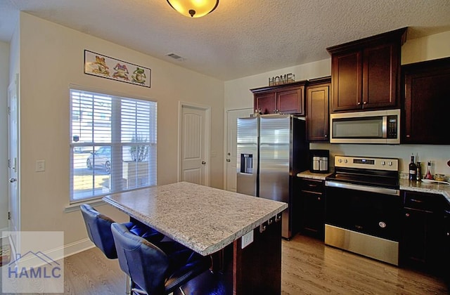 kitchen with light hardwood / wood-style flooring, a textured ceiling, appliances with stainless steel finishes, a kitchen island, and a breakfast bar area