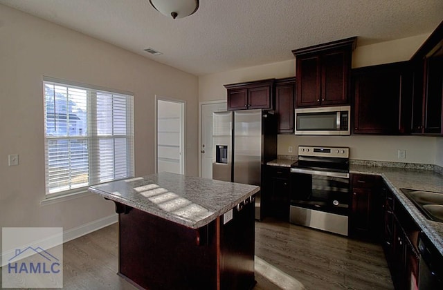 kitchen featuring a breakfast bar, appliances with stainless steel finishes, hardwood / wood-style floors, a center island, and a wealth of natural light