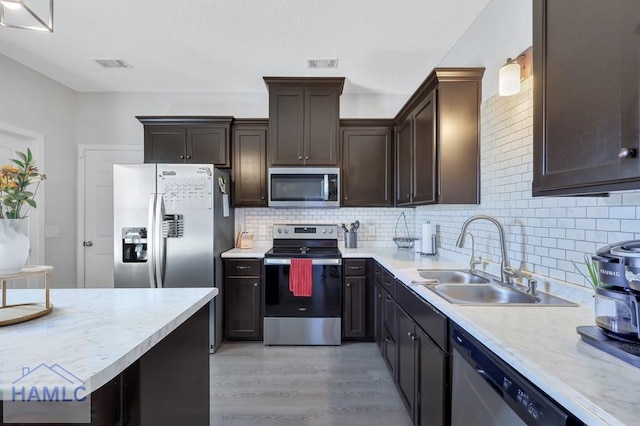 kitchen with appliances with stainless steel finishes, tasteful backsplash, dark brown cabinetry, sink, and light hardwood / wood-style flooring