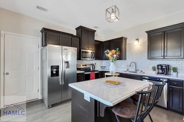 kitchen featuring sink, stainless steel appliances, light hardwood / wood-style flooring, decorative light fixtures, and a kitchen island