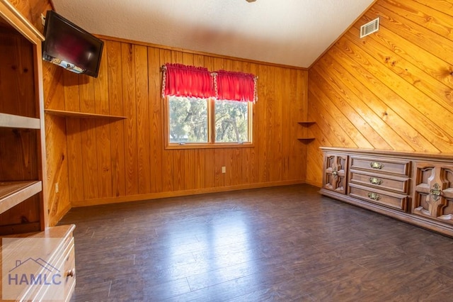 unfurnished room featuring lofted ceiling, visible vents, wood walls, wood finished floors, and baseboards