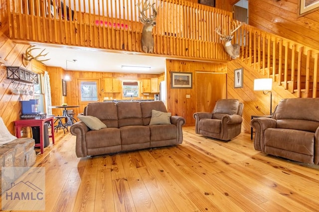 living area featuring wooden walls, light wood-type flooring, stairway, and a high ceiling