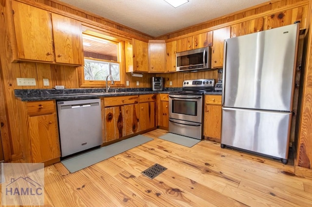 kitchen featuring stainless steel appliances, light wood finished floors, dark countertops, and brown cabinets