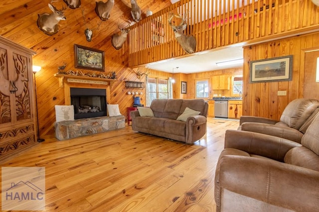 living room with a fireplace with raised hearth, a high ceiling, wood walls, and light wood-style flooring