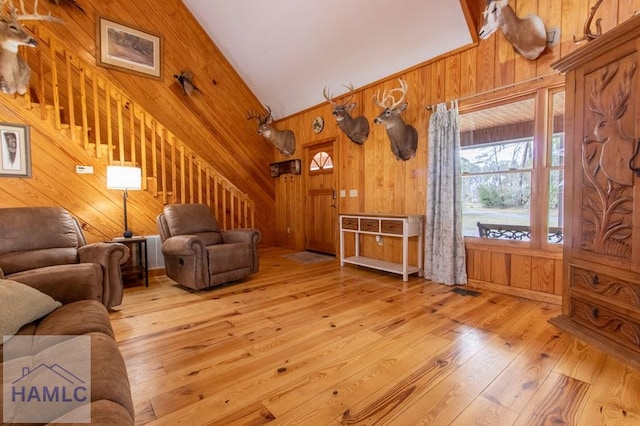 living area featuring vaulted ceiling, stairway, wood-type flooring, and wooden walls