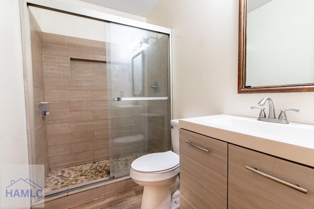 bathroom with vanity, wood finished floors, a shower stall, and toilet