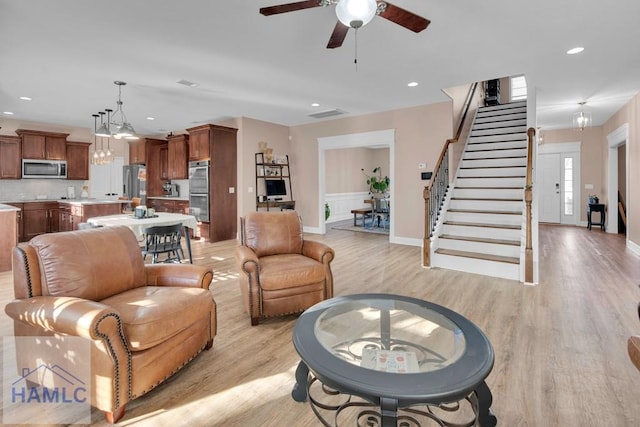 living room featuring ceiling fan with notable chandelier and light hardwood / wood-style flooring