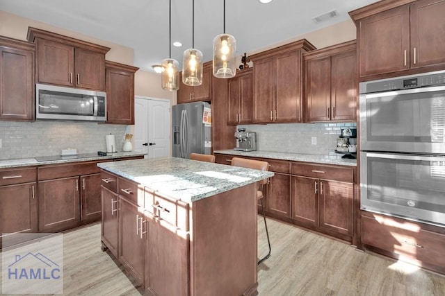 kitchen featuring backsplash, hanging light fixtures, a center island, stainless steel appliances, and light stone countertops