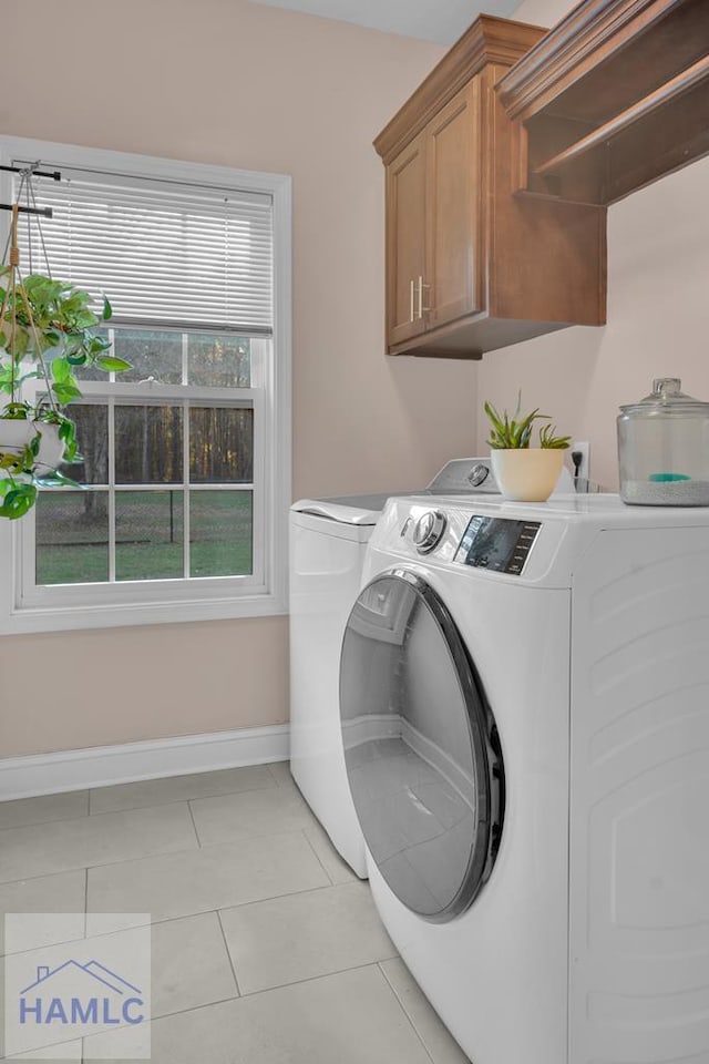 clothes washing area featuring cabinets, washing machine and dryer, and light tile patterned floors