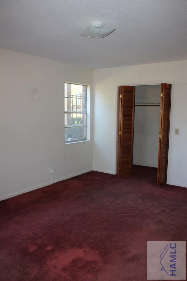 unfurnished bedroom with dark colored carpet, a textured ceiling, and a closet