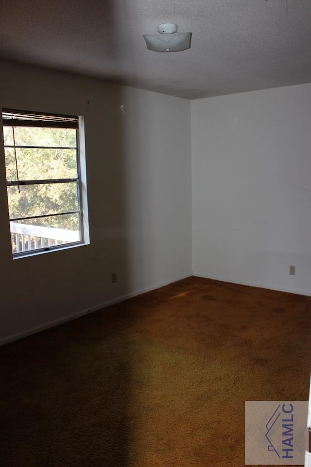 spare room with a textured ceiling and dark colored carpet