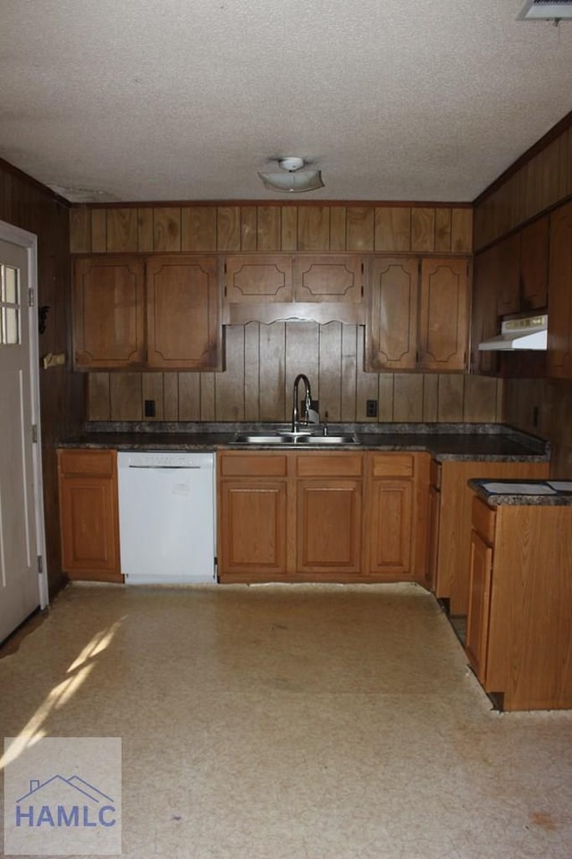 kitchen with wood walls, dishwasher, a textured ceiling, and sink