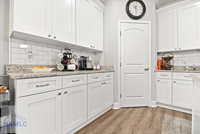 bar featuring backsplash, white cabinetry, light hardwood / wood-style floors, and light stone counters