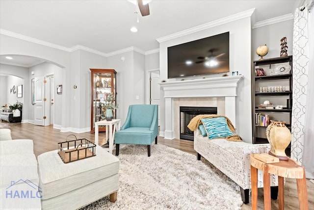 living room with a tile fireplace, ceiling fan, ornamental molding, and hardwood / wood-style flooring