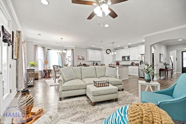 living room with ceiling fan with notable chandelier, a healthy amount of sunlight, ornamental molding, and light hardwood / wood-style flooring