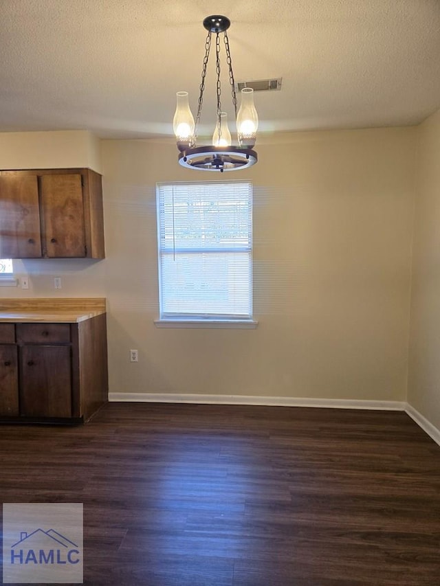 unfurnished dining area with a textured ceiling, an inviting chandelier, and dark hardwood / wood-style floors