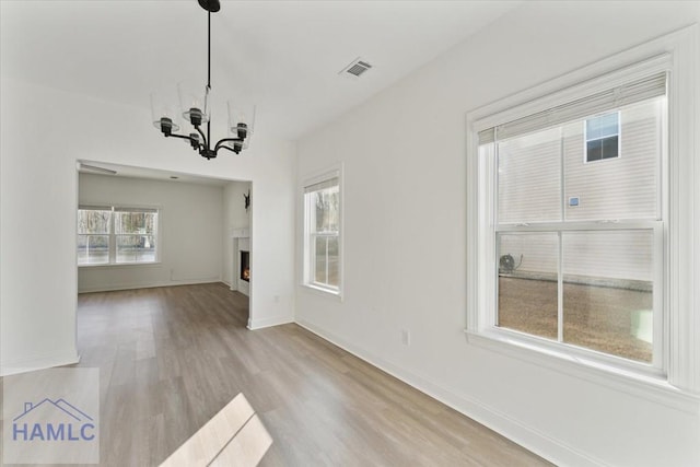 unfurnished living room featuring a warm lit fireplace, baseboards, visible vents, wood finished floors, and a chandelier