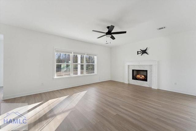 unfurnished living room with baseboards, visible vents, a ceiling fan, a premium fireplace, and wood finished floors