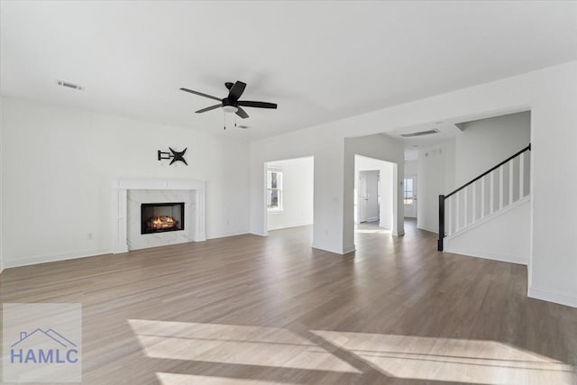 unfurnished living room with stairway, visible vents, wood finished floors, and a high end fireplace