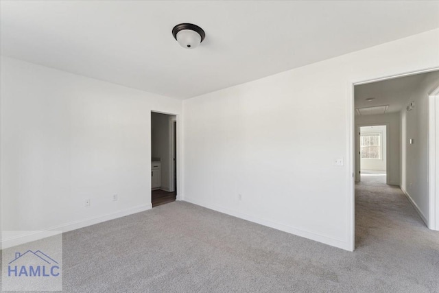 carpeted spare room featuring attic access and baseboards