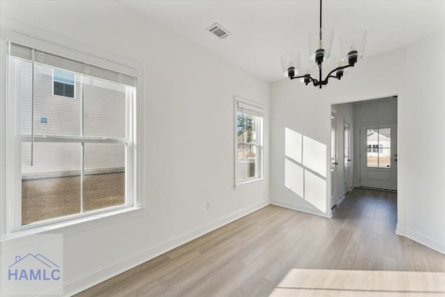 unfurnished dining area with a chandelier, plenty of natural light, wood finished floors, and baseboards