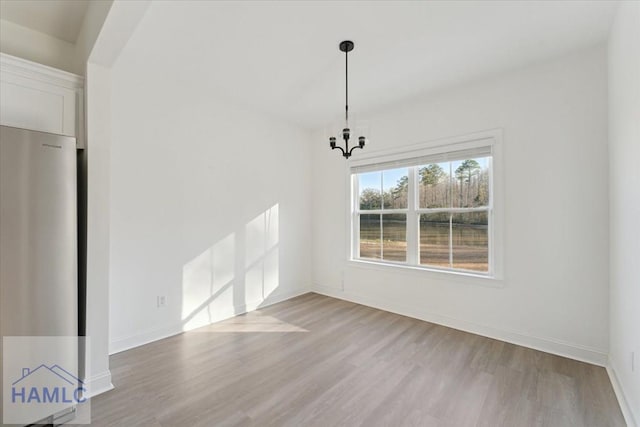 unfurnished dining area featuring a chandelier, baseboards, and wood finished floors