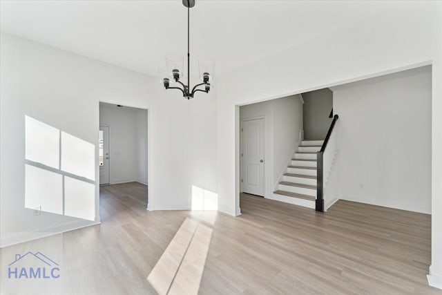 unfurnished dining area featuring a notable chandelier, stairway, and light wood-style floors