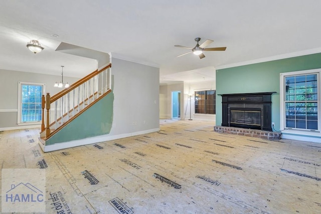 unfurnished living room featuring crown molding, a fireplace, and ceiling fan with notable chandelier