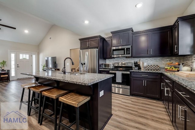 kitchen with lofted ceiling, appliances with stainless steel finishes, a sink, light stone countertops, and a kitchen breakfast bar