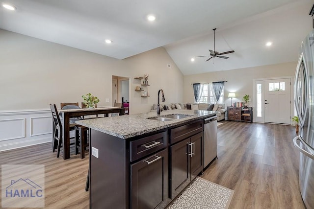 kitchen with light stone counters, appliances with stainless steel finishes, vaulted ceiling, a sink, and dark brown cabinetry