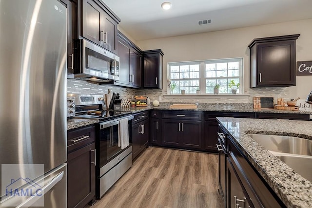 kitchen with light wood-style floors, dark brown cabinets, stainless steel appliances, and decorative backsplash