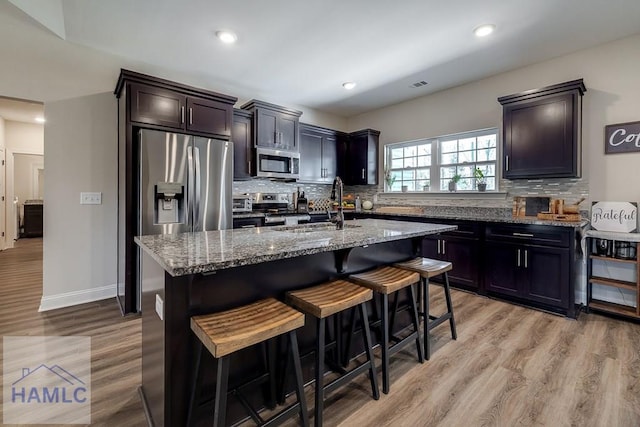 kitchen with stone counters, tasteful backsplash, appliances with stainless steel finishes, a sink, and a kitchen bar