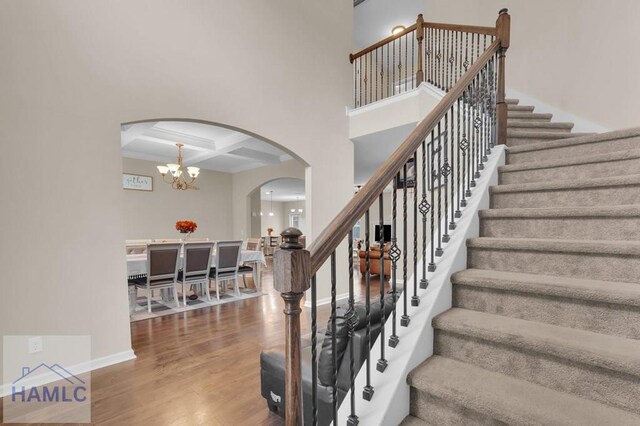 23 Veranda Trl, Midway, GA 31320 - staircase featuring arched walkways, coffered ceiling, wood finished floors, a chandelier, and beam ceiling