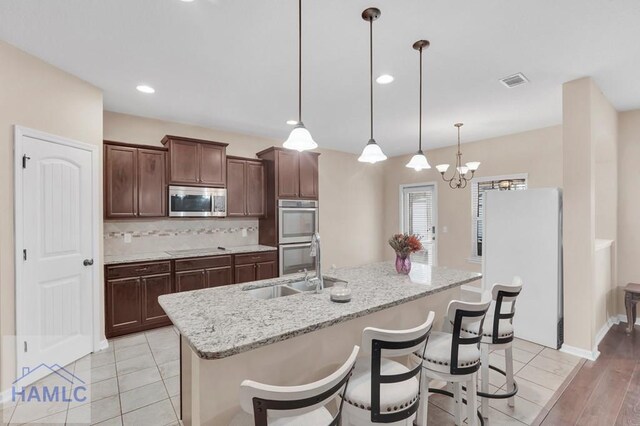 23 Veranda Trl, Midway, GA 31320 - kitchen with stainless steel appliances, tasteful backsplash, an island with sink, dark brown cabinetry, and decorative light fixtures