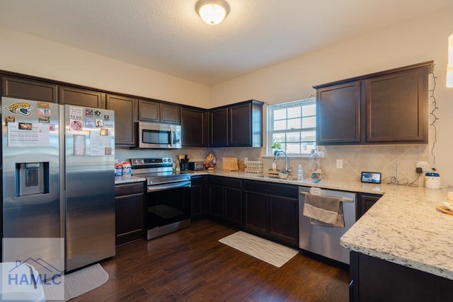 kitchen featuring dark brown cabinetry, tasteful backsplash, dark wood-type flooring, stainless steel appliances, and a sink