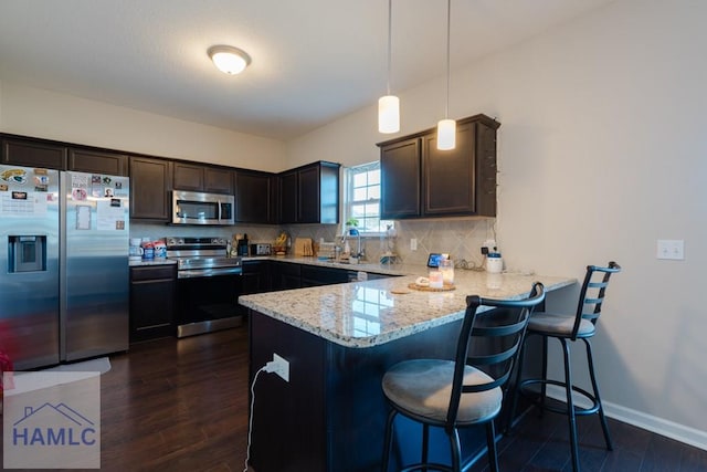 kitchen featuring tasteful backsplash, dark wood finished floors, a peninsula, stainless steel appliances, and a sink