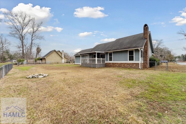 back of house with a fenced backyard, a chimney, a lawn, and brick siding