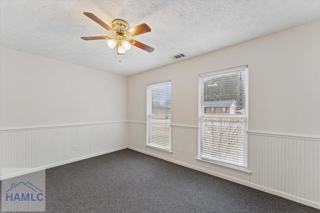 unfurnished room with a wainscoted wall, dark colored carpet, a textured ceiling, and a ceiling fan