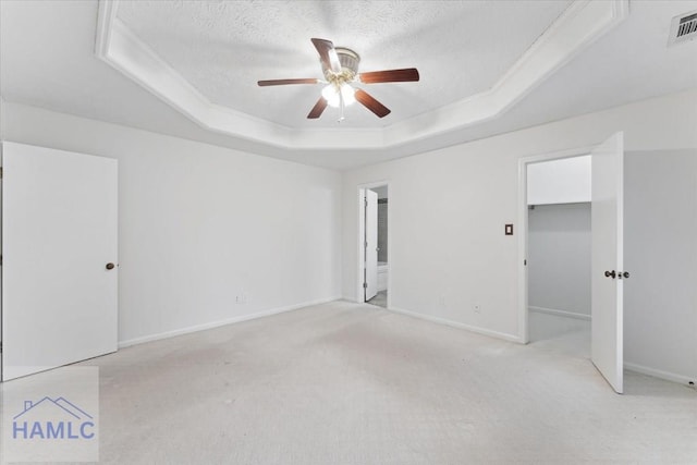 empty room featuring a textured ceiling, a raised ceiling, a ceiling fan, and light colored carpet