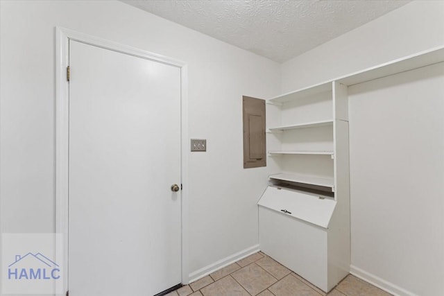 laundry area with a textured ceiling, light tile patterned flooring, electric panel, and baseboards