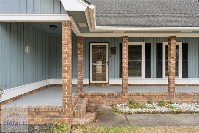 property entrance with board and batten siding, covered porch, brick siding, and a shingled roof