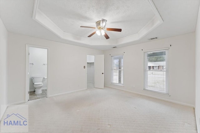 unfurnished room with a textured ceiling, light carpet, a ceiling fan, baseboards, and a raised ceiling