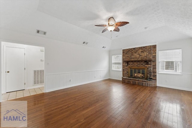 unfurnished living room with a textured ceiling, hardwood / wood-style floors, wainscoting, and visible vents