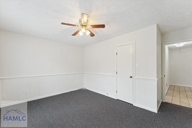 carpeted spare room featuring a wainscoted wall, a ceiling fan, and a textured ceiling