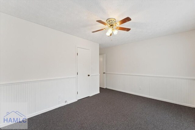 spare room featuring a wainscoted wall, dark colored carpet, a textured ceiling, and a ceiling fan