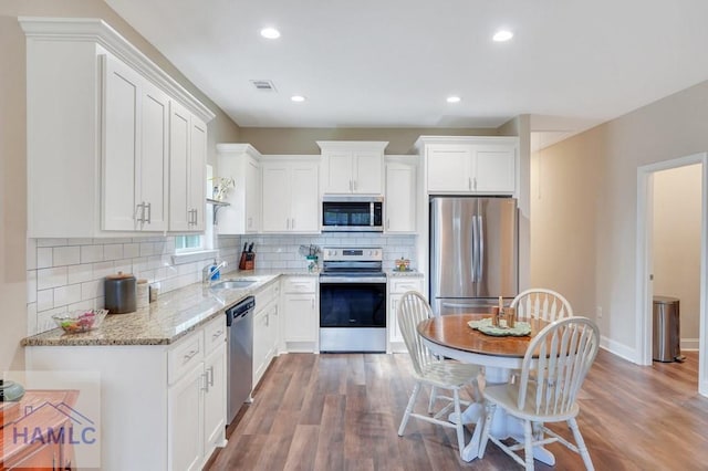 kitchen featuring light stone countertops, white cabinetry, dark hardwood / wood-style flooring, and stainless steel appliances