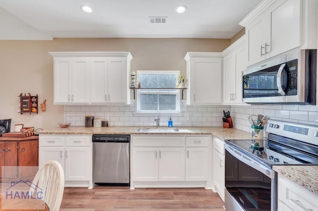 kitchen with white cabinetry, sink, light hardwood / wood-style floors, decorative backsplash, and appliances with stainless steel finishes