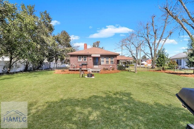 rear view of house featuring a yard, brick siding, fence private yard, and a chimney