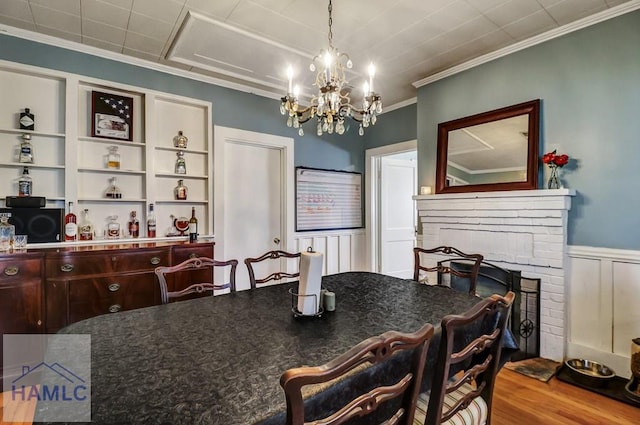 dining area with wood finished floors, an inviting chandelier, wainscoting, crown molding, and a brick fireplace